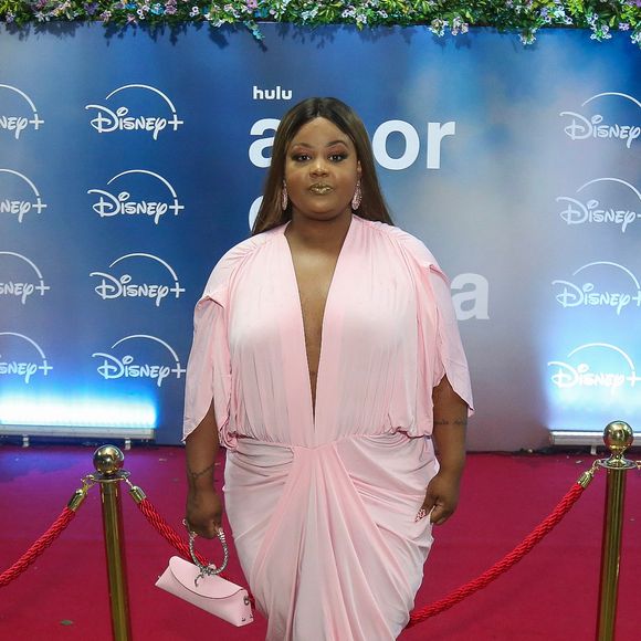 MC Carol: surge com um vestido longo em tom rosa-bebe, marcado por decote profundo em "V", mangas com fendas, drapeado frontal na cintura e bolsa de mão rosa com alça estruturada