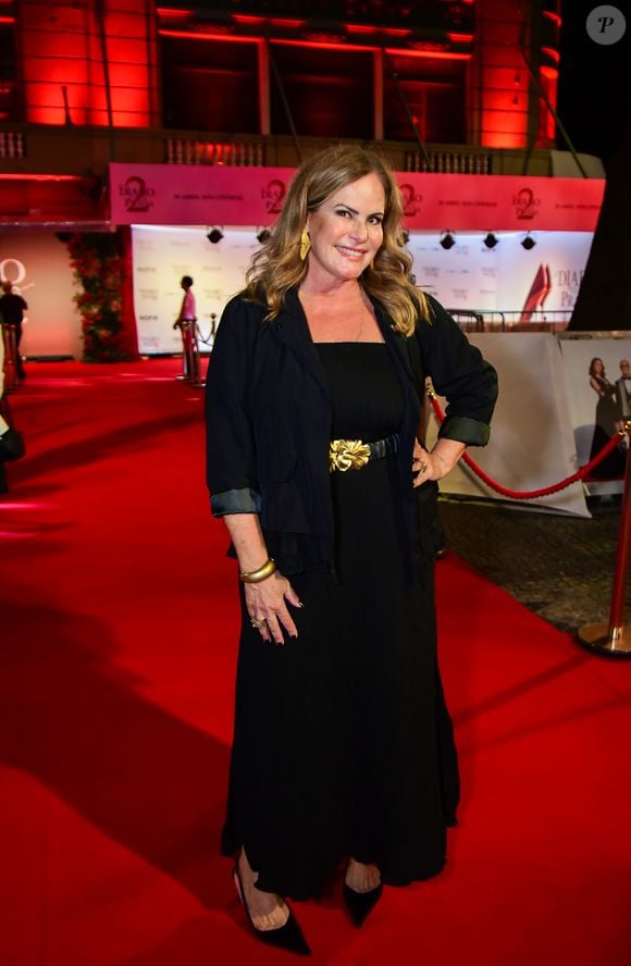 Renata Ceribelli: a jornalista optou por uma elegância sóbria e funcional. Ela utilizou um vestido longo preto de corte reto, sobreposto por um casaco de corte utilitário em tecido leve. O ponto focal do look é o cinto largo com uma fivela de flor dourada, que quebra a monocromia e adiciona um elemento de luxo. Os acessórios - bracelete dourado e brincos geométricos - harmonizam com o metal do cinto