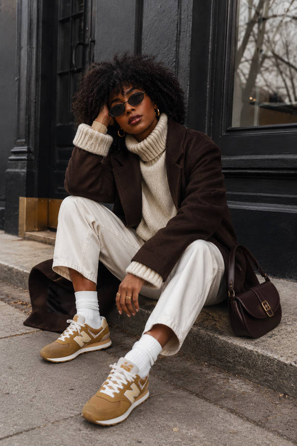 Quer atualizar o guarda-roupa de inverno? Uma das propostas mais modernas para usar o New Balance 574 V2 é combiná-lo com casaco marrom-chocolate, gola alta creme e calça de corte reto. A mistura valoriza o tom caramelo do tênis e deixa a produção ainda mais refinada