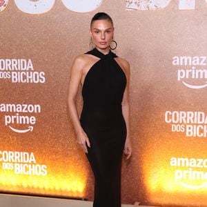 Isis Valverde aposta na elegância minimalista com um vestido longo preto de silhueta ajustada ao corpo, destacando decote frente única transpassado no pescoço e capuz fluido caindo suavemente pelas costas