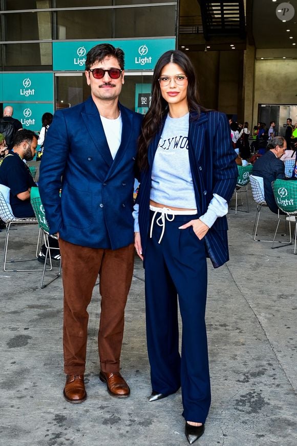 O ator Daniel Rocha veste um blazer transpassado azul-marinho, ajustado ao corpo, que ganha leveza ao ser combinado com uma camiseta branca básica por baixo, deixando o visual menos rígido enquanto Vitória Strada elege calça pantalona azul-marinho fluida mantém a elegância da silhueta, finalizada com maestria por escarpins de bico fino para o Rio2C