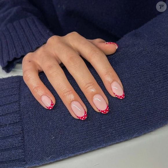 Unhas 2026: Um clássico absoluto: pontas vermelhas com poás brancos sobre base natural. Elegância garantida, especialmente em unhas curtas
