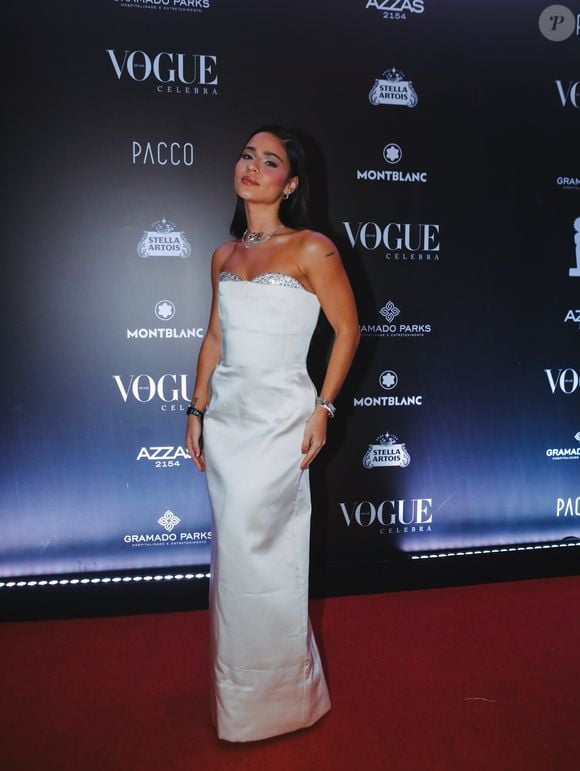 Giullia Buscacio usou um vestido branco tomara que caia, de corte reto e com uma faixa de brilho prateado no busto. Joias prateadas e sandálias metalizadas finalizaram a produção