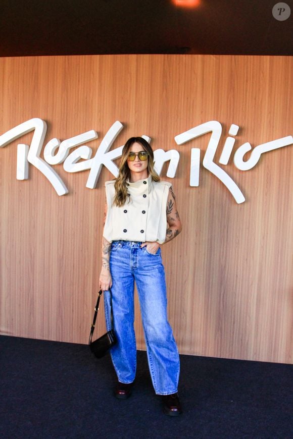 Mari Palma optou por uma blusa sem mangas off-white de gola alta e abotoamento duplo frontal que remete aos cortes de alfaiataria militar. O equilíbrio casual vem com a calça jeans puddle de lavagem clássica e pernas amplas, bolsa de ombro preta estruturada, óculos de sol com lentes amareladas e botas pretas de bico fino