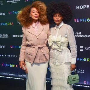 Raissa Santana e sua acompanhante trouxeram uma proposta de alfaiataria romântica e texturizada. Raissa (à esquerda) veste um blazer de tweed rosa seco com botões dourados e amarração na cintura, combinado com uma saia longa fluida em tom off-white. Já a convidada ao seu lado apresenta um visual lúdico com uma camisa branca sob um top estruturado com laços gigantes, finalizado com uma saia de camadas de tule e pérolas, acessórios em tom pastel e sapatos lilás