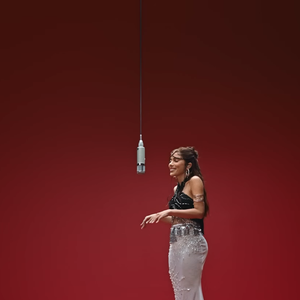 Na parte inferior, o visual equilibra a dramaticidade do topo com uma saia branca de cintura baixa bordada, que adiciona leveza e textura por meio de aplicações brilhantes e transparências sutis