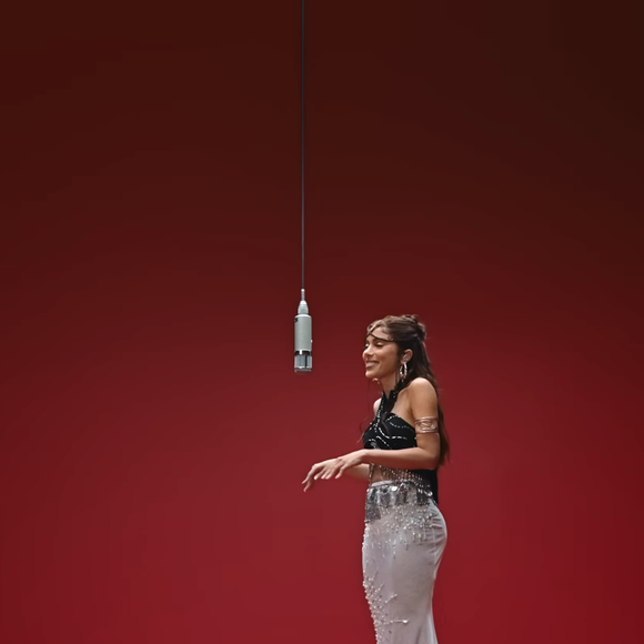 Na parte inferior, o visual equilibra a dramaticidade do topo com uma saia branca de cintura baixa bordada, que adiciona leveza e textura por meio de aplicações brilhantes e transparências sutis