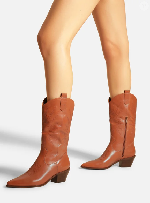 O modelo apresenta cano médio, salto baixo bloco de 4,6 cm e bico fino, além de bordados western no cano e no cabedal. As tiras laterais facilitam o calce, enquanto o fechamento em zíper interno garante mais praticidade no dia a dia