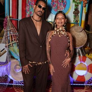 O casal Mell Muzzillo e Marcello Melo Jr surgiu em sintonia com tons terrosos e referências ancestrais. Mell veste um longo marrom em tecido texturizado que se molda ao corpo, adornado com um colar maximalista de sementes e búzios que envolve todo o pescoço e colo. Marcello complementa a estética com um conjunto de blazer e calça em marrom escuro, utilizado sem camisa e finalizado com um cinto e colar de contas