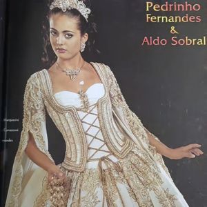 8. Vestido dourado

Um verdadeiro momento da moda nupcial do início dos anos 2000. O vestido traz um corpete estruturado em tom off-white, com aplicações em dourado que seguem um desenho rococó luxuoso. A parte central é marcada por um trançado de fitas douradas, que alonga a silhueta e reforça a ideia de cintura marcada. As mangas são estilo cape, totalmente rendadas e bordadas com arabescos dourados, transmitindo uma imponência quase real. 

A saia volumosa ganha destaque com bordados em arabescos florais, criando um contraste entre opulência e delicadeza. O look é finalizado com uma tiara robusta cravejada de pedrarias, brincos e colar maximalistas, o auge da estética rainha barroca que dominava os editoriais de noiva da época.