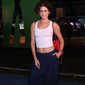 Laura Fernandez: A modelo desfilou um visual despojado e de cintura baixa, combinando uma regata cropped branca básica de canelado fino a uma calça jeans oversized escura de modelagem bem ampla com pregas frontais. O ponto de cor maximalista ficou por conta da bolsa de ombro vermelha em couro matelassê com alça de corrente