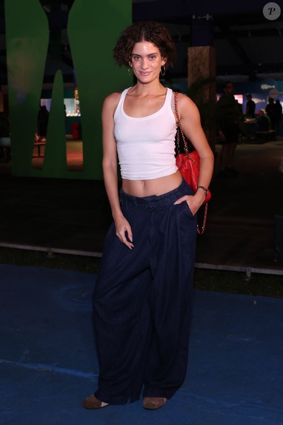 Laura Fernandez: A modelo desfilou um visual despojado e de cintura baixa, combinando uma regata cropped branca básica de canelado fino a uma calça jeans oversized escura de modelagem bem ampla com pregas frontais. O ponto de cor maximalista ficou por conta da bolsa de ombro vermelha em couro matelassê com alça de corrente