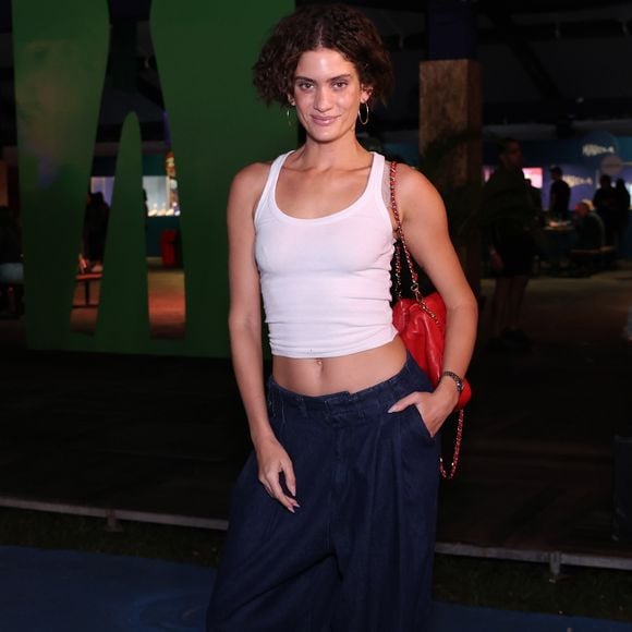 Laura Fernandez: A modelo desfilou um visual despojado e de cintura baixa, combinando uma regata cropped branca básica de canelado fino a uma calça jeans oversized escura de modelagem bem ampla com pregas frontais. O ponto de cor maximalista ficou por conta da bolsa de ombro vermelha em couro matelassê com alça de corrente