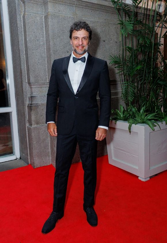 Rodrigo Lombardi segue o rigor do traje de gala clássico, utilizando um smoking (black tie) de corte slim fit. O conjunto é composto por um paletó de um único botão com lapelas de cetim em formato 'shawl' (gola xale), camisa social branca impecável com botões ocultos e gravata borboleta preta tradicional