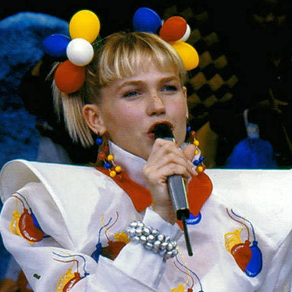 Xuxa no 'Xou da Xuxa' com seu visual criativo, colorido e irreverente, com ombreiras, e as famosas xuxinhas de cabelo bem chamativas.