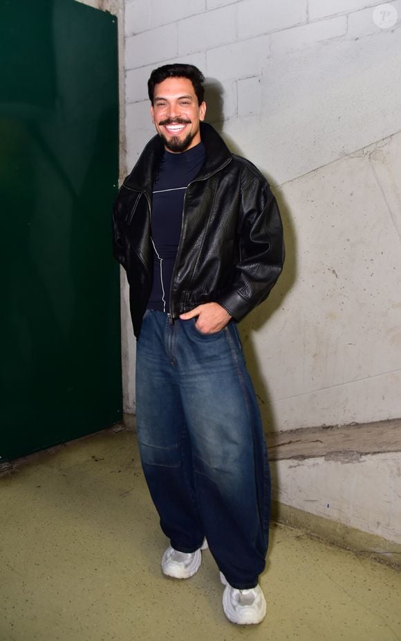 O ex-BBB Vinicius apostou na estética streetwear de inspiração noventista ao vestir uma jaqueta de couro preta em modelagem puffer. Por baixo, usou uma blusa azul-marinho de gola alta e combinou com calça jeans wide leg de lavagem azul-escura com recortes