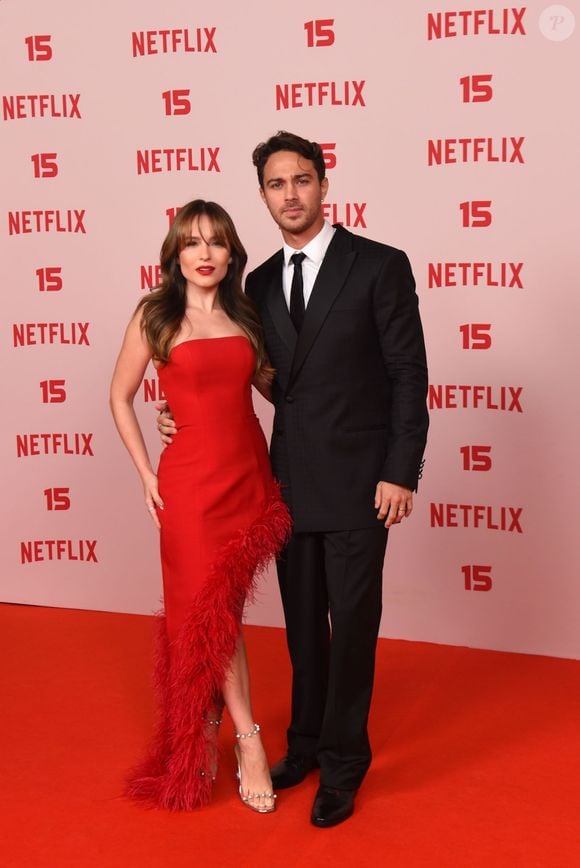 Larissa Manoela e André Luiz Frambach: Larissa surge num vestido cai-cai vermelho vibrante de corte ajustado, destacado por uma aplicação assimétrica de plumas na mesma cor que desce do quadril até à barra, acompanhada por sandálias prateadas de salto; André opta por um fato clássico preto de corte estruturado com gravata escura e camisa branca