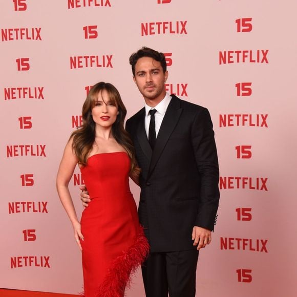 Larissa Manoela e André Luiz Frambach: Larissa surge num vestido cai-cai vermelho vibrante de corte ajustado, destacado por uma aplicação assimétrica de plumas na mesma cor que desce do quadril até à barra, acompanhada por sandálias prateadas de salto; André opta por um fato clássico preto de corte estruturado com gravata escura e camisa branca