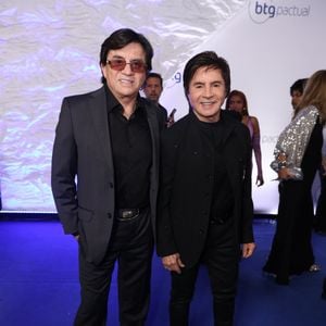 Chitãozinho e Xororó: Chitãozinho (à esquerda) veste terno cinza-chumbo sobre camisa social preta aberta no colarinho, finalizado com cinto de fivela dourada trabalhada. Xororó (à direita) optou por um blazer preto de gola padre com sutis pontos de brilho, sobre blusa preta de gola alta e calça skinny