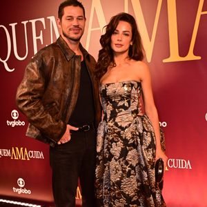 José Loreto e Fernanda Marques: o casal coordenou estilos com texturas marcantes; José Loreto escolheu uma jaqueta de couro marrom com efeito envelhecido sobre uma base totalmente preta de camiseta e jeans, mantendo uma estética urbana. Já Fernanda Marques surgiu em um vestido tomara-que-caia de jacquard com padronagem floral em tons metálicos de bronze e prata, apresentando um volume estruturado nos quadris e uma clutch preta oval