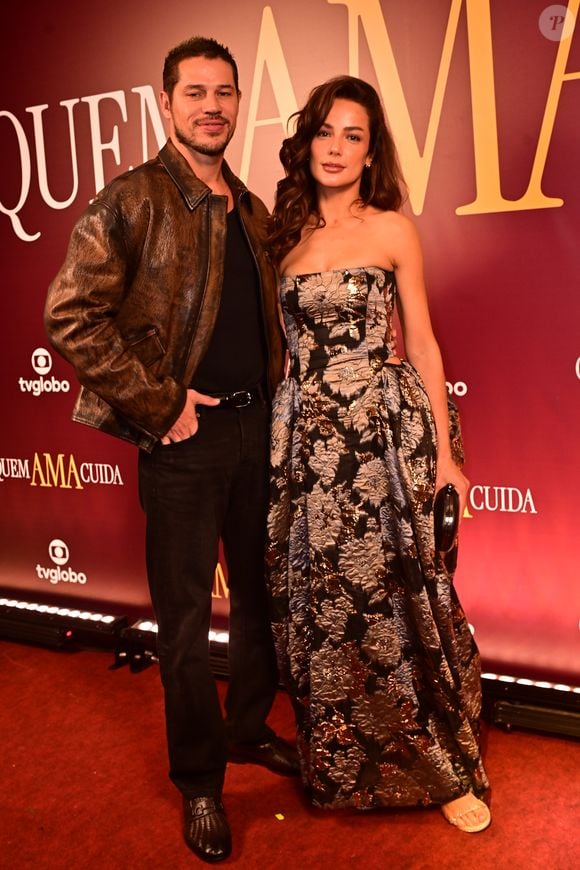 José Loreto e Fernanda Marques: o casal coordenou estilos com texturas marcantes; José Loreto escolheu uma jaqueta de couro marrom com efeito envelhecido sobre uma base totalmente preta de camiseta e jeans, mantendo uma estética urbana. Já Fernanda Marques surgiu em um vestido tomara-que-caia de jacquard com padronagem floral em tons metálicos de bronze e prata, apresentando um volume estruturado nos quadris e uma clutch preta oval