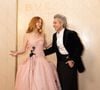 Marina Ruy Barbosa exibe uma estética romântica-subversiva ao vestir um imponente vestido midi em tom rosa-pastel, estruturado com um corpete de decote reto e alças finas que deságua em uma volumosa saia de renda floral e tule; Ao seu lado, Alexandre Nero adota uma releitura moderna do black tie, combinando um refinado paletó de veludo preto com uma camisa social branca de botões escuros - usada elegantemente desabotoada no colarinho -, uma expressiva faixa de alfaiataria na cintura adornada por um broche dourado e calças pretas de corte amplo (wide leg)