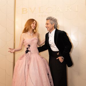Marina Ruy Barbosa exibe uma estética romântica-subversiva ao vestir um imponente vestido midi em tom rosa-pastel, estruturado com um corpete de decote reto e alças finas que deságua em uma volumosa saia de renda floral e tule; Ao seu lado, Alexandre Nero adota uma releitura moderna do black tie, combinando um refinado paletó de veludo preto com uma camisa social branca de botões escuros - usada elegantemente desabotoada no colarinho -, uma expressiva faixa de alfaiataria na cintura adornada por um broche dourado e calças pretas de corte amplo (wide leg)