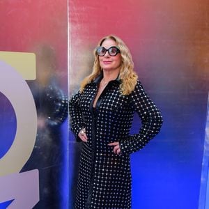 Vera Fischer: esbanjando elegância e modernidade, Vera Fischer utilizou um sobretudo longo de couro preto que funciona como a peça central do look. O casaco apresenta uma padronagem quadriculada formada por pequenas aplicações metálicas ou cristais refletivos em toda a sua extensão, criando um efeito de brilho pontuado. Por baixo, nota-se uma base preta lisa