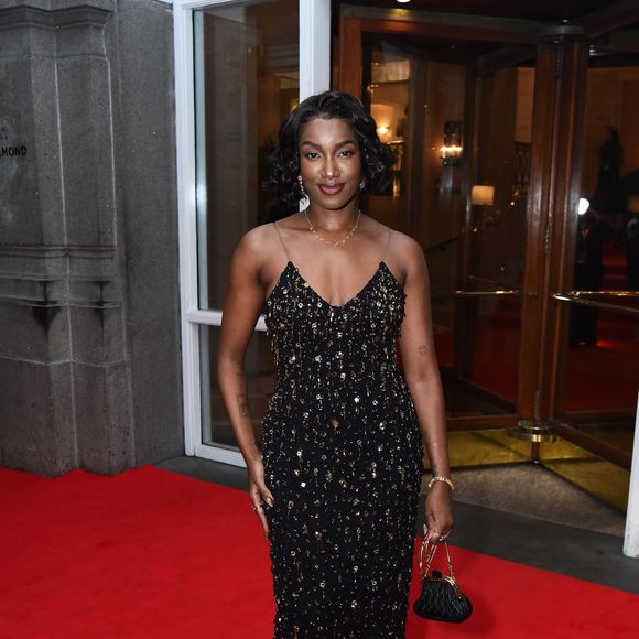 Iza entregou pura sofisticação com um vestido coluna preto inteiramente bordado com cristais e paetês dourados. O brilho da peça é estratégico, criando um efeito de 'chuva de ouro' sob as luzes do evento. Com alças finíssimas e decote sutil, o modelo valoriza a silhueta de forma clássica e poderosa. Iza complementou a produção com uma mini bag de mão em couro matelassê preto e joias minimalistas, mantendo o foco no trabalho manual do vestido e no seu cabelo curto em ondas estilo vintage