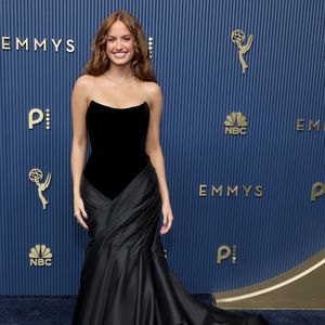 Haley Kalil: vestido longo tomara que caia na cor preta, composto por um corpete em veludo fosco de decote suavemente curvado e saia ajustada em cetim fluído. O design destaca um drapeado assimétrico na altura dos quadris que se estende até o chão em uma cauda fluida. O visual é finalizado com um delicado colar de brilhantes e cabelos ondulados soltos
