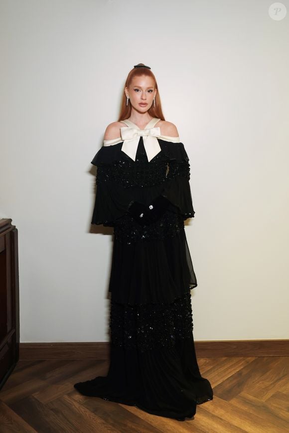 Marina Ruy Barbosa elegeu um vestido preto longo com mangas volumosas, aplicações brilhantes e detalhes de transparência. O look também conta com um grande laço branco no colo e uma pequena cauda