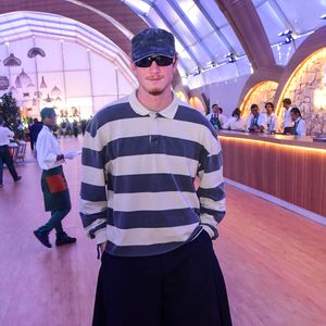 Pedro Novaes aposta em uma camisa polo de mangas compridas e modelagem oversized com listras horizontais largas em cinza e off-white, combinada com uma bermuda de alfaiataria preta super ampla de caimento plissado. O toque moderno fica por conta do boné estonado, óculos escuros com lente espelhada, meias altas na cor mostarda e mocassins pretos envernizados