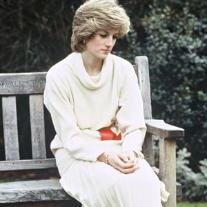 Bem antes do fim do casamento com o atual Rei Charles, príncipe na época, Diana já fazia uso de botas no seu dia a dia, como mostram registros da Princesa de Gales usando um suéter creme de gola alta e saia plissada com cinto e botas vermelhas. Ela aparece sentada em um banco de madeira no jardim de sua residência no Palácio de Kensington, em 14 de dezembro de 1983, em Londres, Reino Unido.