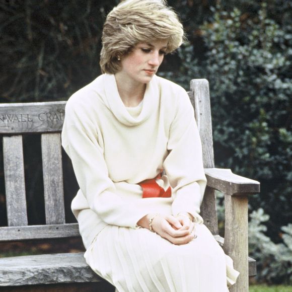 Bem antes do fim do casamento com o atual Rei Charles, príncipe na época, Diana já fazia uso de botas no seu dia a dia, como mostram registros da Princesa de Gales usando um suéter creme de gola alta e saia plissada com cinto e botas vermelhas. Ela aparece sentada em um banco de madeira no jardim de sua residência no Palácio de Kensington, em 14 de dezembro de 1983, em Londres, Reino Unido.