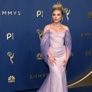 Florence Pugh surgiu em uma proposta romântica e dramática com um vestido longo em tom lilás de efeito levemente cintilante. A peça traz decote reto estruturado, mangas bufantes e caídas em tule transparente e uma saia sereia com cauda esvoaçante do mesmo tecido. O look foi arrematado por um colar gargantilha marcante com pedrarias coloridas, coque alto conceitual e beleza em tons neutros