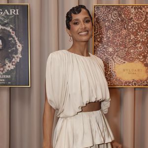 O visual de Camila Pitanga ganha ares de alta-costura com um sofisticado penteado de ondas esculpidas (finger waves) bem coladas à cabeça, brincos pendentes de pedrarias e sapatos de salto dourados que pontuam a paleta neutra e refinada