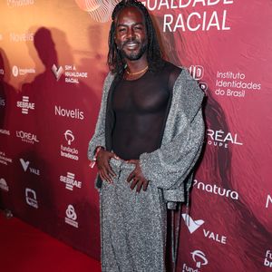 Jonathan Azevedo apostou no brilho e na fluidez para o tapete vermelho. O ator veste um conjunto de calça oversized e casaco tipo jaqueta, ambos confeccionados em um tecido prateado com textura de paetês miúdos que garantem movimento. Por baixo, uma blusa de tule preto com transparência revela a silhueta, trazendo um toque de sensualidade