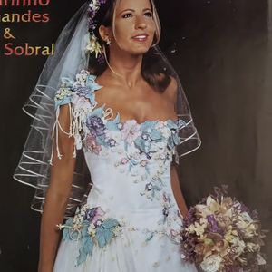 6. Vestido floral colorido

Uma explosão de romantismo! Aqui o branco é apenas a tela de fundo para aplicações em 3D de flores lilás, azuis e rosadas, criando um efeito de jardim encantado. O corpete é justo e trabalhado, enquanto a saia ganha movimento com as flores que descem até a barra. O buquê combina com os tons do vestido, e a tiara floral completa a estética campestre. Em 2002, esse vestido era considerado visionário e lúdico, trazendo cor para o altar e continua perfeito para quem deseja fugir do clássico branco em 2025.