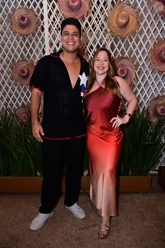 Guilherme e Letícia Tavares: ele vestiu uma camisa de tricô preta de mangas curtas com pontos abertos, gola polo e detalhes em linha vermelha e branca na lapela, além de calça preta e tênis brancos. Ela usou um vestido midi de cetim em efeito degradê que flui do tom vinho ao champanhe, com decote frente única e sandálias dourada