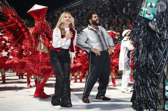 Juliana Baroni desfilou usando um look mais clássico, com calça preta brilhante, camisa branca e um colete vermelho brilhante