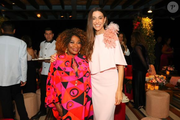 Mônica Martelli usa vestido rosa-claro com capa fluida e flores 3D no ombro durante evento do Outubro Rosa 2026; Zezé Motta também esteve presente