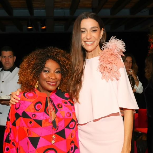 Mônica Martelli usa vestido rosa-claro com capa fluida e flores 3D no ombro durante evento do Outubro Rosa 2026; Zezé Motta também esteve presente