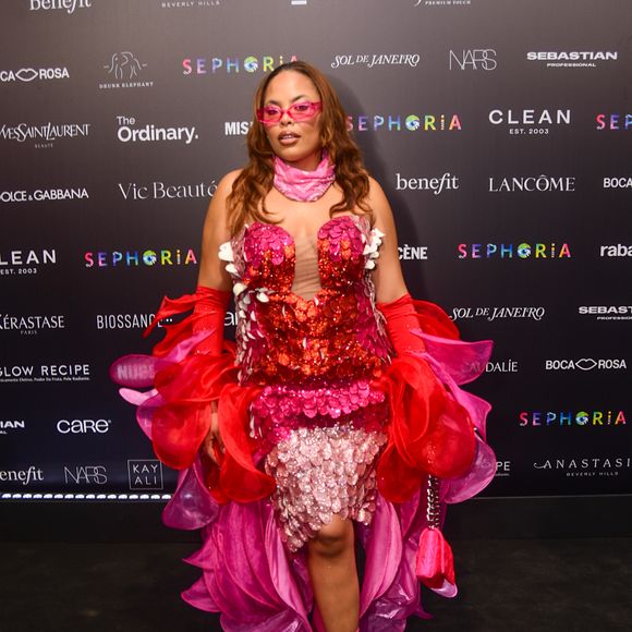 Rita Carreira optou por um visual maximalista e floral, vestindo uma peça estruturada que simulava camadas de pétalas em tons de vermelho, rosa e lilás, decorada com paetês. A modelo elevou a complexidade do look com luvas vermelhas de babados volumosos, uma bandana rosa no pescoço e óculos de sol translúcidos, criando uma composição rica em camadas e texturas