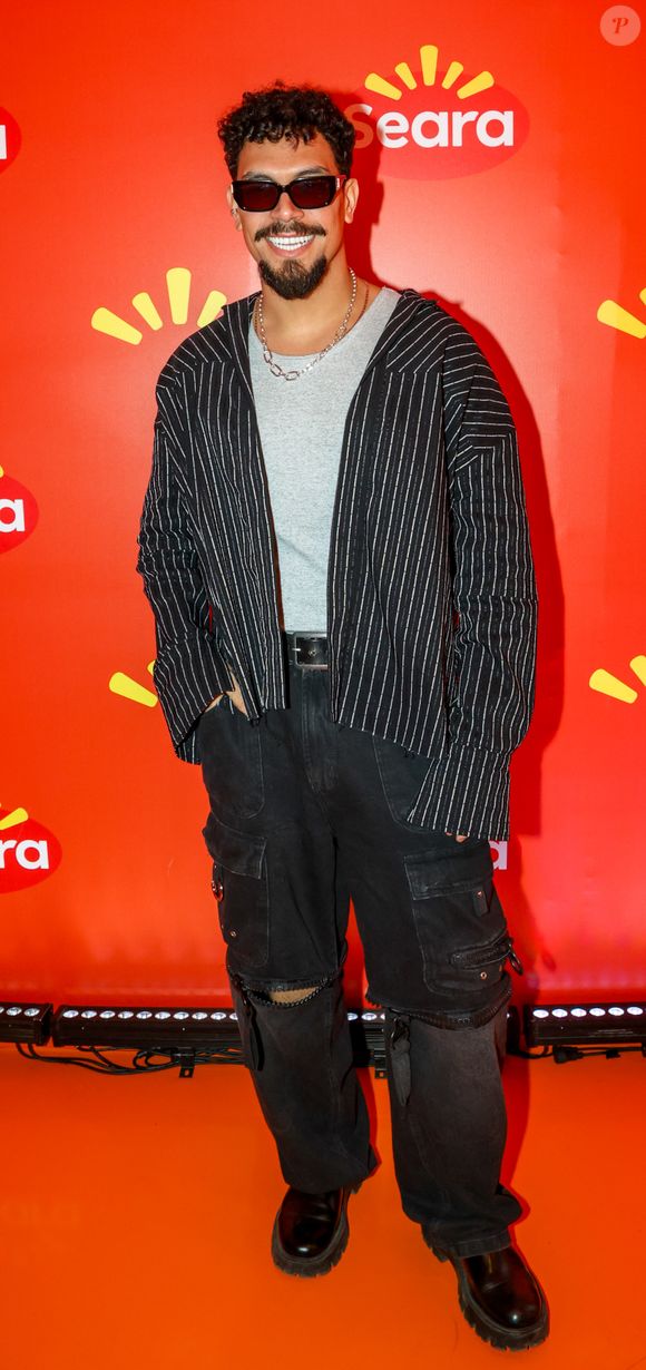O ex-BBB Vinicius usou uma calça jeans rasgada no joelho, uma blusa branca e outra de manga comprida com listras por cima