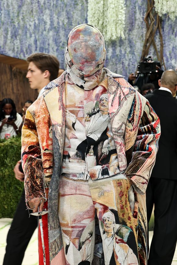 Miles Chamley-Watson A$AP elevou o conceito de arte vestível ao surgir completamente coberto por um conjunto de tapeçaria que reproduzia obras clássicas. Além do casaco e calças coordenados, Rocky utilizou uma máscara integral feita do mesmo tecido tramado, ocultando totalmente sua face e criando uma silhueta contínua que transformou o artista em uma galeria itinerante de texturas e cores