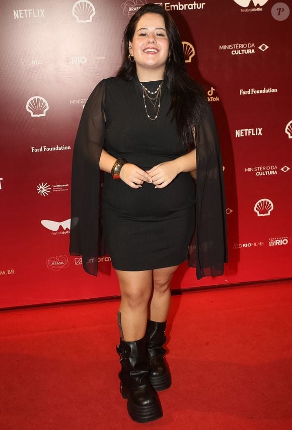 Karol Lannes apostou em um vestido preto curto com mangas transparentes, complementado por colares dourados e botas pretas de solado tratorado