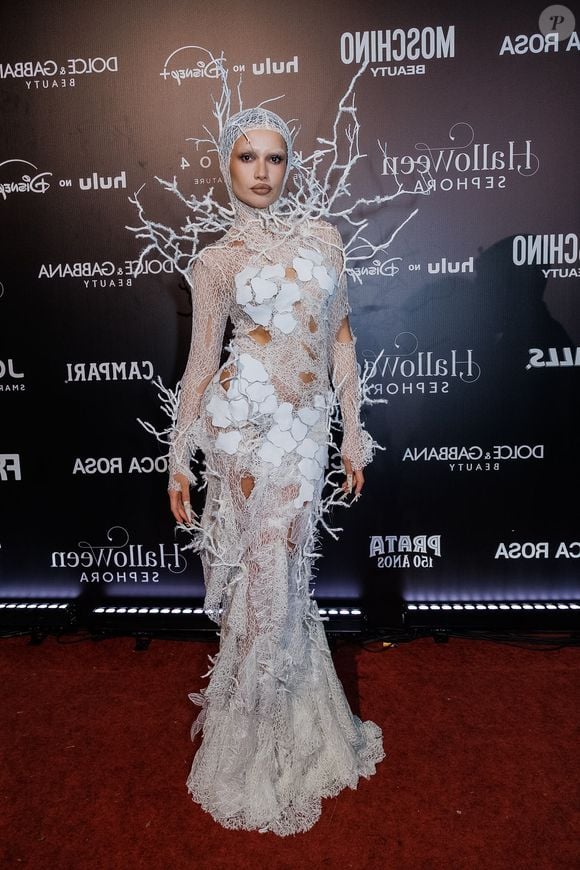 Juliette traz um vestido longo sereia em renda/tricô branco com textura teia de aranha e aplicações de folhas brancas vazadas. O figurino estende-se em uma touca que cobre a cabeça, conectada a uma estrutura tridimensional de galhos secos e cristalizados em tom branco que emolduram os ombros e as costas. O visual traz unhas postiças longas e pontiagudas e maquiagem neutra com lábios contornados