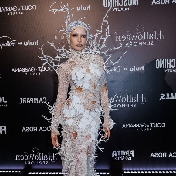 Juliette traz um vestido longo sereia em renda/tricô branco com textura teia de aranha e aplicações de folhas brancas vazadas. O figurino estende-se em uma touca que cobre a cabeça, conectada a uma estrutura tridimensional de galhos secos e cristalizados em tom branco que emolduram os ombros e as costas. O visual traz unhas postiças longas e pontiagudas e maquiagem neutra com lábios contornados