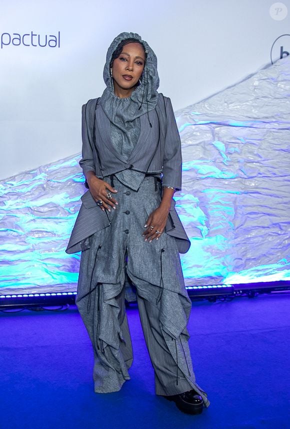 Negra Li: Look conceitual em alfaiataria desconstruída cinza risca-de-giz. Visual composto por blazer cropped de mangas 3/4 sobreposto a um colete assimétrico e calça oversized de modelagem utilitária ampla com amarrações, cordões suspensos e capuz acoplado cobrindo a cabeça