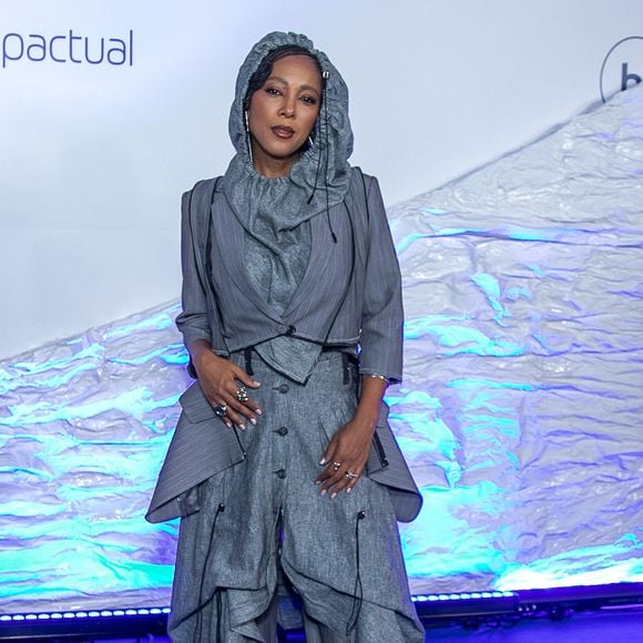 Negra Li: Look conceitual em alfaiataria desconstruída cinza risca-de-giz. Visual composto por blazer cropped de mangas 3/4 sobreposto a um colete assimétrico e calça oversized de modelagem utilitária ampla com amarrações, cordões suspensos e capuz acoplado cobrindo a cabeça